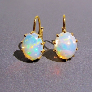 Pode incluir: Um par de brincos de ouro com pedras preciosas de opala de forma oval. As opalas têm uma base branca com cores arco-íris iridescentes.