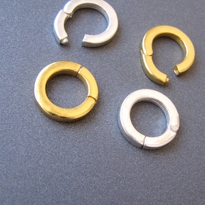 May include: Four jump rings, two silver and two gold, are arranged on a gray surface. The rings are open and ready to be used for jewelry making.