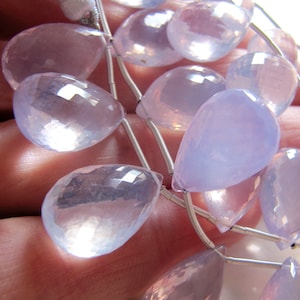 May include: A strand of pale pink and lavender gemstone beads, each bead is faceted and shaped like a teardrop. The beads are strung on silver wire and have a tassel at the top.