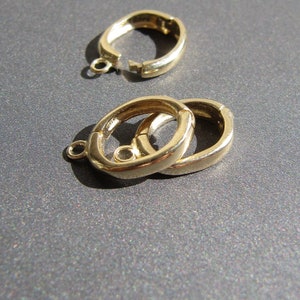 Op de afbeelding: Twee goudkleurige metalen sluitingen voor het maken van sieraden. De sluitingen zijn ovaalvormig en hebben een veerbelaste sluiting.