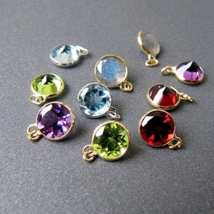 May include: Assortment of gemstone pendants with gold accents. The pendants feature various colors, including green, blue, purple, and red.