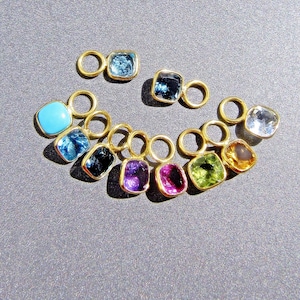 Può includere: Un set di 10 ciondoli in oro con pietre preziose di diversi colori. I ciondoli sono a forma quadrata e hanno un piccolo anello nella parte superiore. Le pietre preziose sono turchese, topazio blu, zaffiro, ametista, zaffiro rosa, peridoto, citrino e quarzo trasparente.