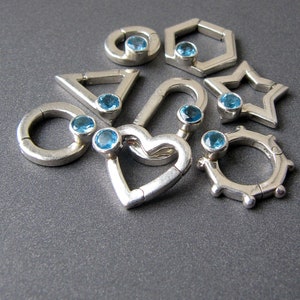 May include: A set of silver charm pendants with blue gemstones in various geometric shapes, including a heart, a circle, a star, a triangle, and a hexagon.