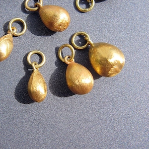 以下が含まれることがあります： ジャンプリングが付いた、金色の涙滴型のペンダントが7つ集まったものです。ペンダントは表面がテクスチャ加工されています。