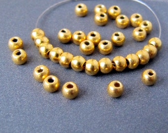 May include: A close-up of a string of gold beads, with some beads scattered around it. The beads are round and have a smooth, shiny finish.