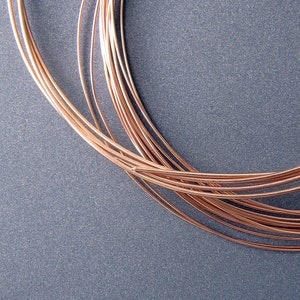May include: A close-up of a bundle of copper wire, coiled in a circular shape, against a gray background.