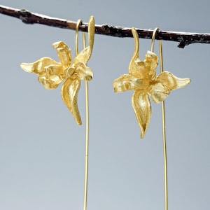 May include: A pair of gold-toned earrings with delicate flower-shaped charms hanging from long, thin wires.