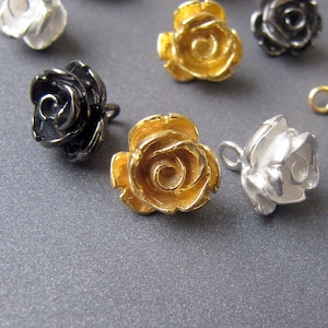 May include: Assortment of rose-shaped metal charms in gold, silver, and black. The charms are detailed with a raised, textured rose design.