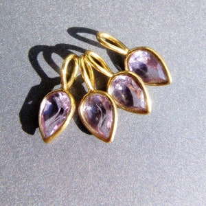 Könnte beinhalten: Fünf goldene Anhänger mit Amethyststeinen in Tropfenform. Die Anhänger sind fächerförmig angeordnet.
