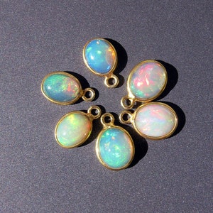 May include: Seven oval-shaped opal gemstones with gold settings. The opals are iridescent with shades of blue, green, and pink.
