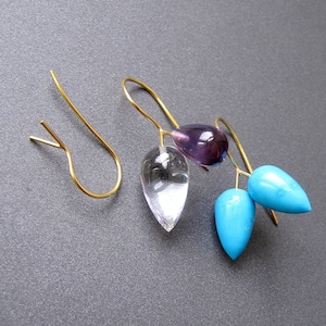 May include: A pair of gold earrings with three teardrop-shaped stones. The stones are clear, purple, and turquoise.