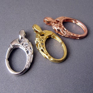 May include: Three ornate oval-shaped clasps in silver, gold, and rose gold. Each clasp has a delicate filigree design.