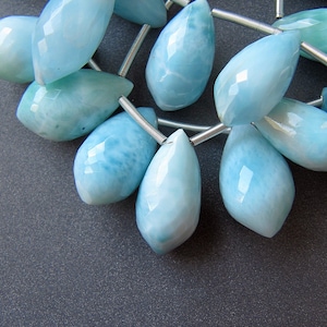 May include: A strand of light blue gemstone beads with a faceted teardrop shape. The beads are strung on silver wire.