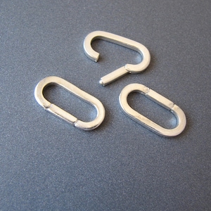 May include: Three silver metal oval-shaped jump rings. The rings are open and have a smooth finish.