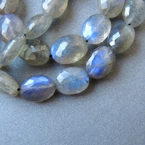 May include: A strand of oval-shaped labradorite beads with a blue iridescent sheen. The beads are strung on a black cord.