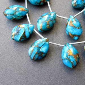 Op de afbeelding: Een streng turquoise en gouden edelsteen kralen in een druppelvorm. De kralen zijn geregen op een zilveren draad.