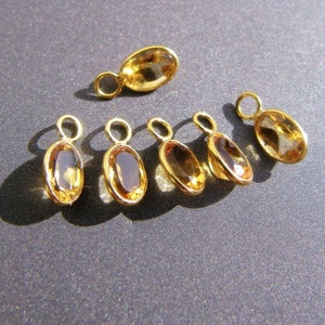 May include: Seven gold-toned oval-shaped charms with clear amber gemstones. Each charm has a small loop for attaching to a necklace or bracelet.