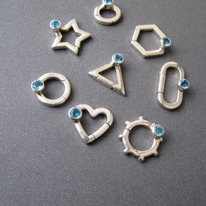 May include: Ten silver charms with blue gemstones, each charm is a different geometric shape: circle, star, heart, hexagon, triangle, and oval.