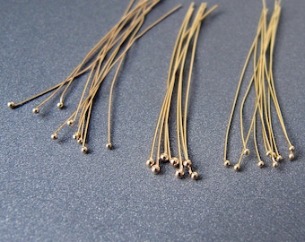 May include: Three bundles of gold-colored head pins with round heads. The pins are arranged in a row on a gray surface.