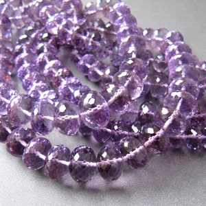May include: A strand of amethyst beads, faceted and polished, with a light purple hue. The beads are strung on a clear thread and are arranged in a loose pile.