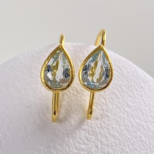 May include: A pair of drop earrings featuring faceted, pear-shaped light blue gemstones set in gold-toned metal. Each earring has a curved wire hook attachment, showcasing a clear, translucent stone with a pointed bottom and a rounded top.