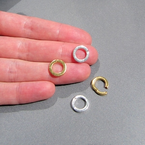 May include: Four silver and gold jump rings, a type of jewelry finding, are shown on a hand. The jump rings are open and ready to be used in jewelry making.