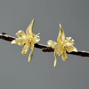 Op de afbeelding: Een paar gouden oorringen in de vorm van een bloem. De oorringen zijn delicaat en ingewikkeld, met een getextureerd oppervlak. Ze zijn perfect om elke outfit een vleugje elegantie te geven.