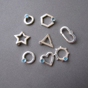 May include: A set of ten silver charms with blue gemstones. The charms are shaped like a star, heart, circle, hexagon, triangle, and a few other abstract shapes.