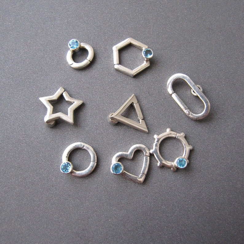 May include: A set of ten silver charms with blue gemstones. The charms are shaped like a star, heart, circle, hexagon, triangle, and a few other abstract shapes.