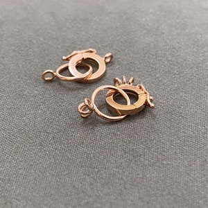 May include: Two gold-toned metal clasps for jewelry making. Each clasp has two interlocking circles.