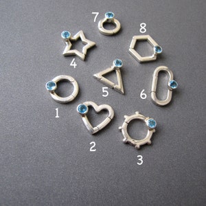 May include: Eight silver charms with blue gemstones. Each charm is a different shape: circle, heart, star, triangle, hexagon, and three more circles with different designs.