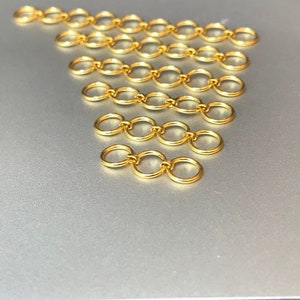 May include: A set of gold jump rings, arranged in a triangular pattern, on a silver surface. The jump rings are all the same size and are connected together in a chain-like fashion.