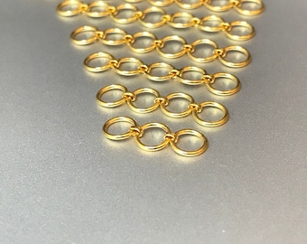 May include: A set of gold jump rings, arranged in a triangular pattern, on a silver surface. The jump rings are all the same size and are connected together in a chain-like fashion.