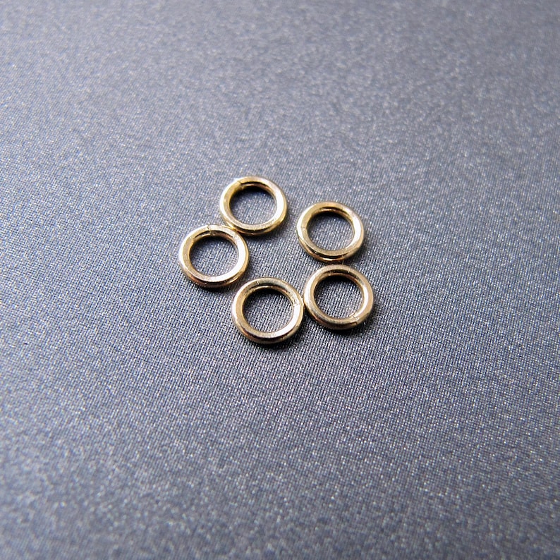 May include: Six gold jump rings, arranged in a circle pattern on a gray background.