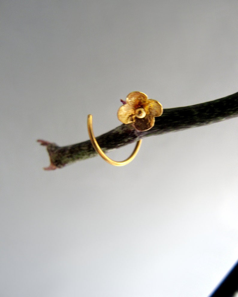 K&ouml;nnte beinhalten: Ein goldener Ohrring in Bl&uuml;tenform mit einem einfachen Kreisdesign. Der Ohrring h&auml;ngt an einem Zweig.