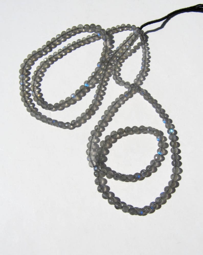 May include: A strand of gray labradorite beads with iridescent blue and green flashes. The beads are strung on a black cord and are approximately 6mm in diameter.