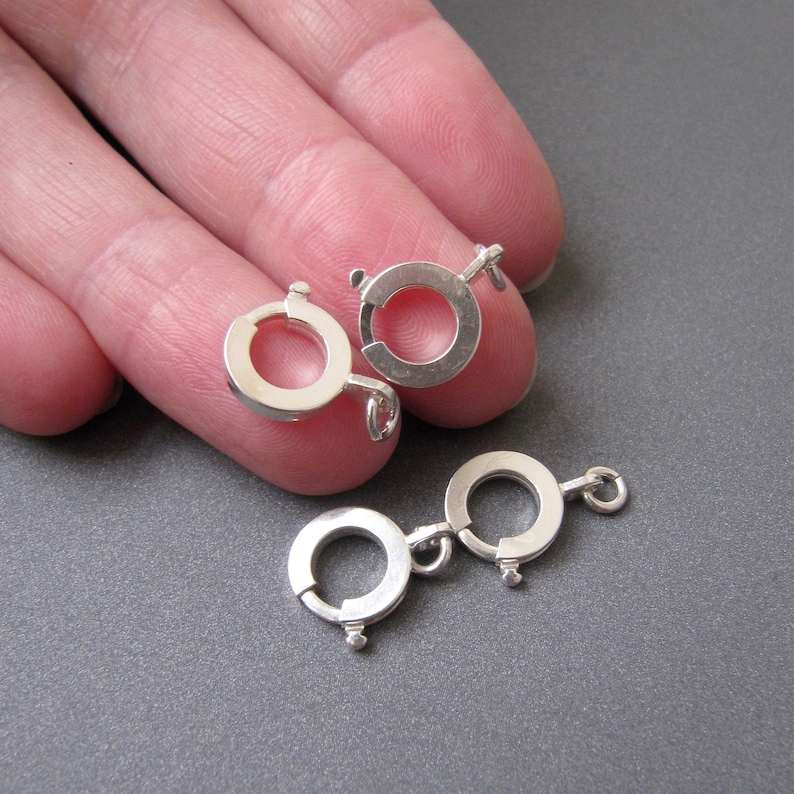 Op de afbeelding: Twee zilverkleurige metalen sluitingen voor het maken van sieraden. Elke sluiting heeft een ronde ring met een veerbelaste sluiting.