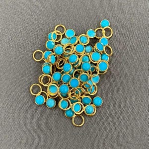 May include: A pile of turquoise blue gemstone beads with gold jump rings. The beads are round and have a smooth, polished finish.