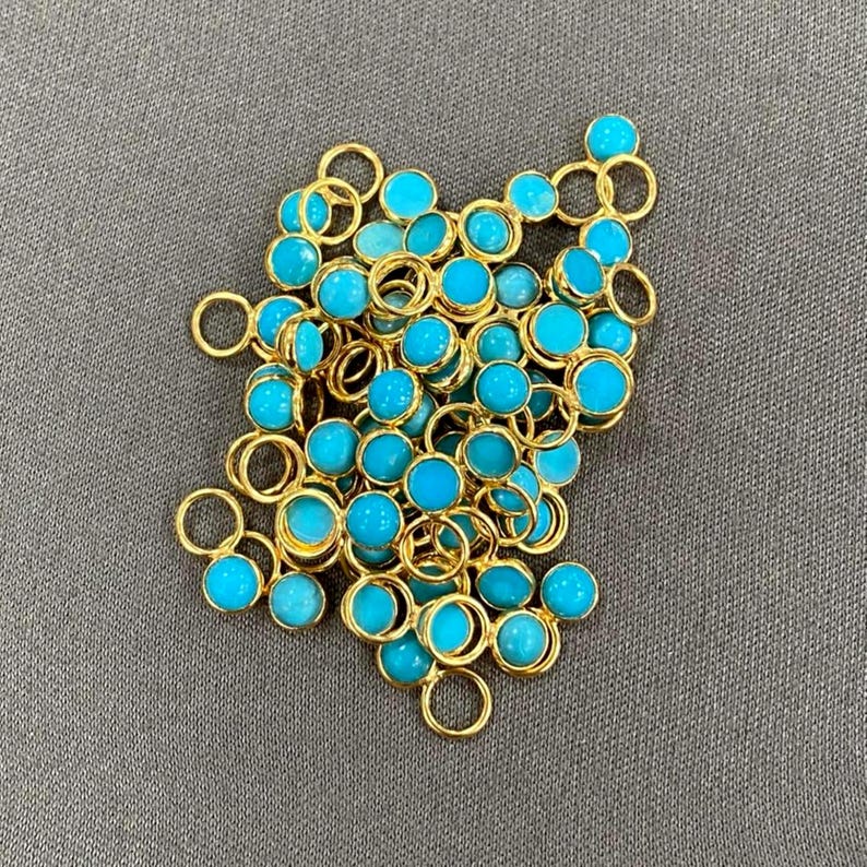 May include: A pile of turquoise blue gemstone beads with gold jump rings. The beads are round and have a smooth, polished finish.