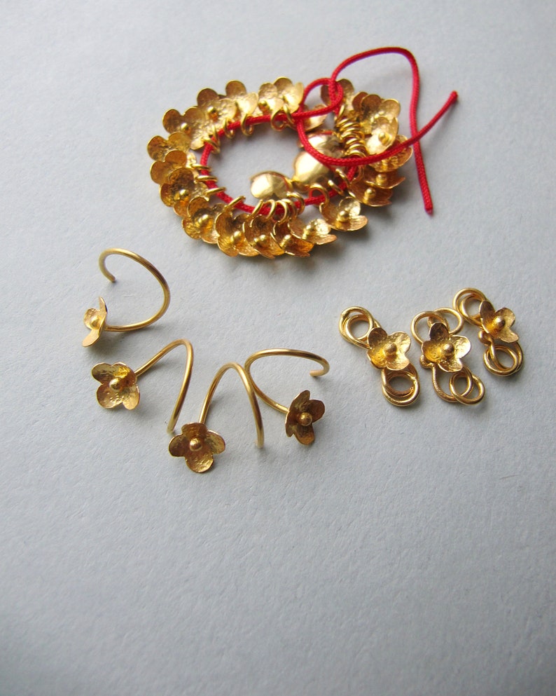 K&ouml;nnte beinhalten: Ein Set aus goldfarbenen Schmuckst&uuml;cken, darunter ein bl&uuml;tenf&ouml;rmiger Anh&auml;nger, ein Paar Ohrringe und drei bl&uuml;tenf&ouml;rmige Verbindungselemente.