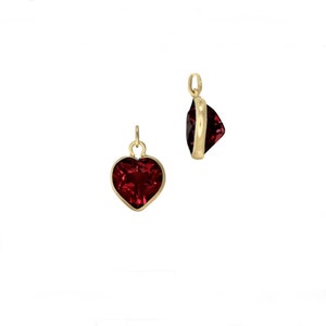 May include: A gold heart charm featuring a red gemstone. The charm is ideal for adding a touch of sparkle to any jewellery project.
