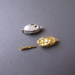 May include: Three gold-toned jewelry clasps. One clasp is a silver-toned oval with the text "Jewelers Collection" and a small red stone. The second clasp is a flower-shaped design. The third clasp is a small, thin, straight piece.