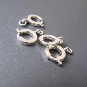 Op de afbeelding: Vier zilverkleurige metalen sluitingen voor het maken van sieraden. Elke sluiting heeft een ronde vorm met een scharnierende opening.