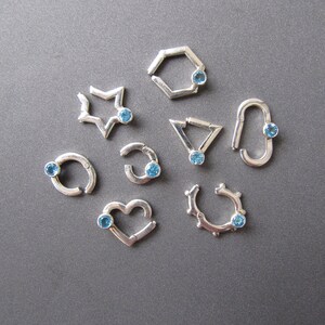 May include: Nine silver rings with blue gemstones. Each ring has a different shape, including a star, a heart, a circle, a pentagon, and a triangle.