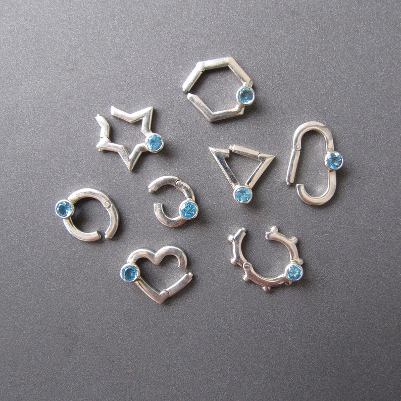 May include: Nine silver rings with blue gemstones. Each ring has a different shape, including a star, a heart, a circle, a pentagon, and a triangle.