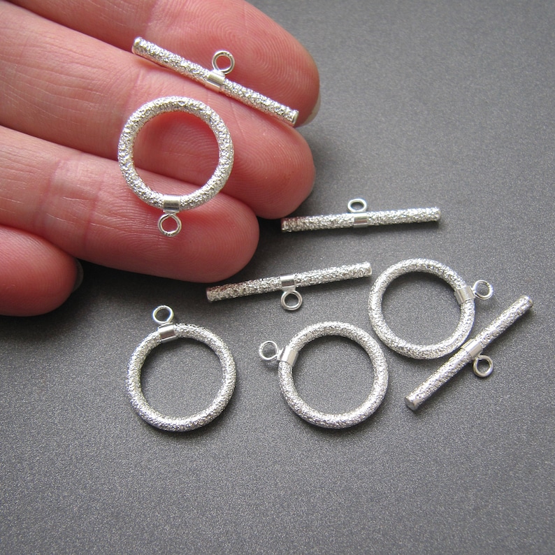 May include: Silver toggle clasps with textured finish. The clasps are in the shape of a circle and a bar. The clasps are used for jewelry making.