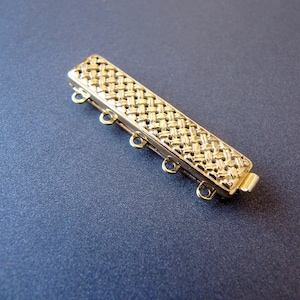 Pode incluir: Extensor de metal dourado com um padrão tecido e cinco argolas de salto. O extensor mede aproximadamente 5 cm de comprimento.