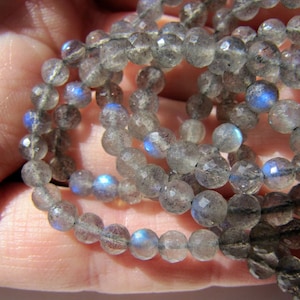 May include: A strand of gray faceted labradorite beads with iridescent blue flashes. The beads are round and have a smooth, polished finish.