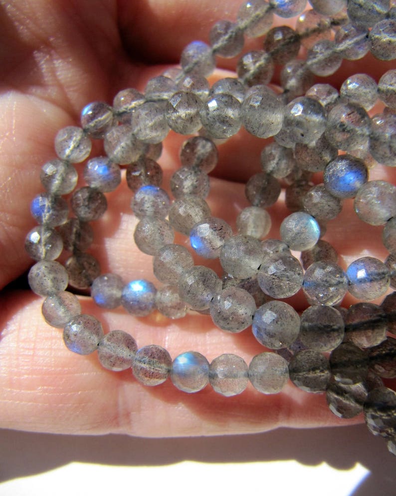 May include: A strand of gray faceted labradorite beads with iridescent blue flashes. The beads are round and have a smooth, polished finish.