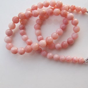Op de afbeelding: Een streng roze opaal kralen, elke kraal is gefacetteerd en heeft een licht verschillende roze tint.